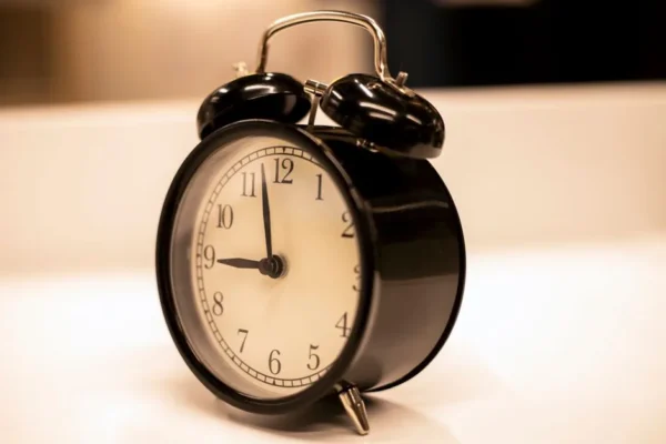 Close-up of a classic black analogue alarm clock on a desk with a serene background.