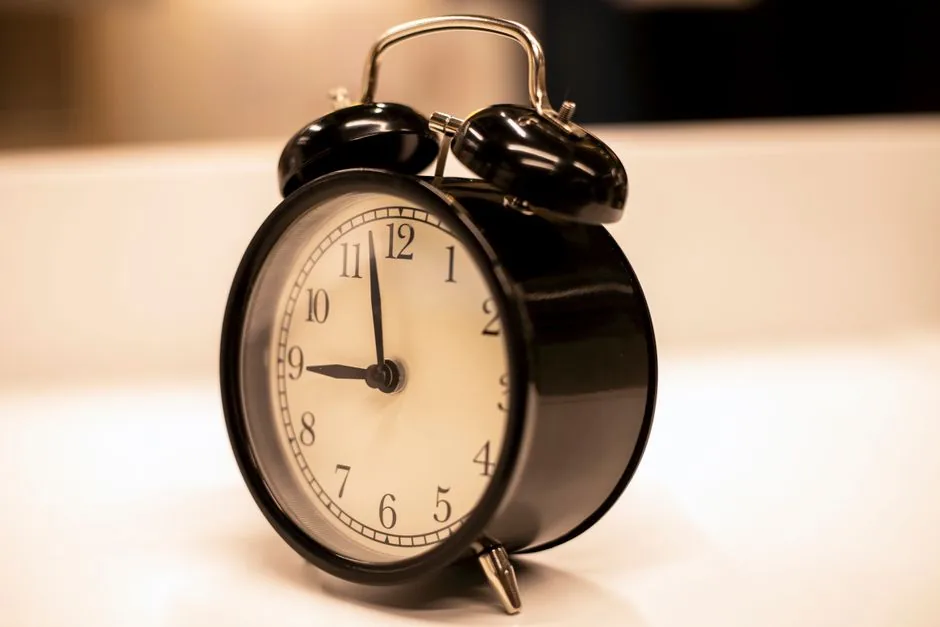 Close-up of a classic black analogue alarm clock on a desk with a serene background.