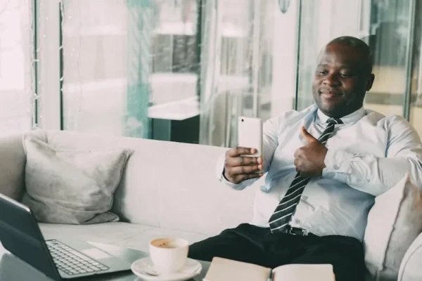 Confident businessman thumbs up during a video call in a relaxed office setting.